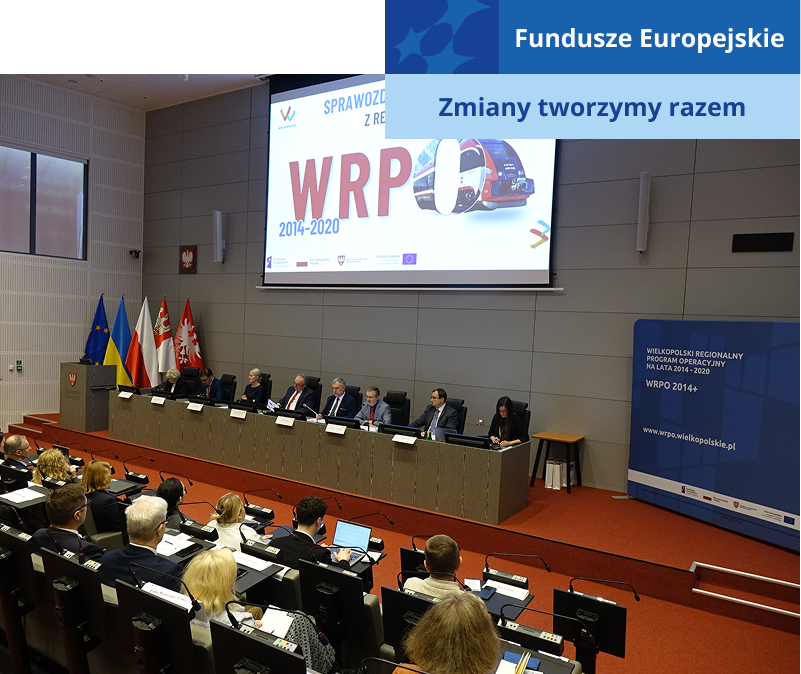 Zdjęcie wykonano w sali audytoryjnej. Na scenie, za długim pulpitem siedzi osiem osób. Nad nimi znajduje się ekran z napisem: Sprawozdanie końcowe z realizacji WRPO 2014-2020. Wśród publiczności znajduje się kilkadziesiąt osób. Każdy ma do dyspozycji własny pulpit z mikrofonem. Fotografia pochodzi z archiwum Urzędu Marszałkowskiego Województwa Wielkopolskiego.
