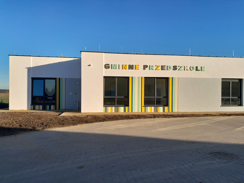 Zdjęcie przedstawia gmach nowego przedszkola. To parterowy budynek z kolorowym napisem „gminne przedszkole”. Fotografia pochodzi z archiwum beneficjenta.