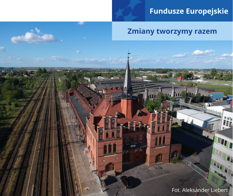 Fotografia z lotu ptaka przedstawia dworzec kolejowy, przypominający nieco w swojej budowie pałac – ma strzelistą wieżę, jest z czerwonej cegły. Z lewej znajdują się tory kolejowe, po prawej zaś zabudowania miejskie. Autorem zdjęcia jest Aleksander Liebert.