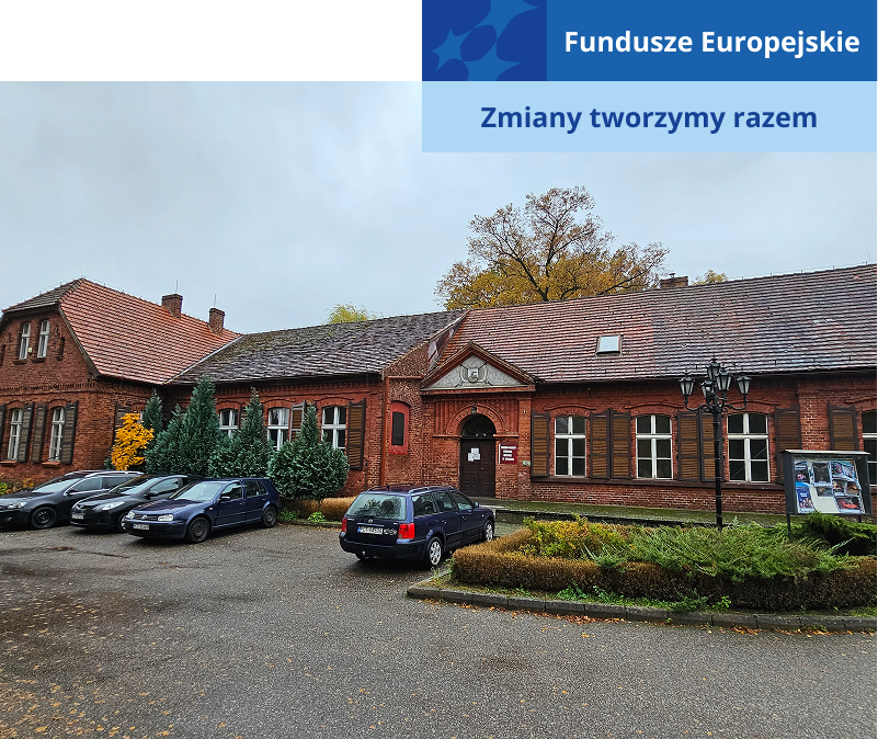 Zdjęcie przedstawia niski, szeroki budynek z cegły, ze spadzistym dachem. Na parkingu przed nim stoją samochody. Fotografia pochodzi z archiwum beneficjenta.