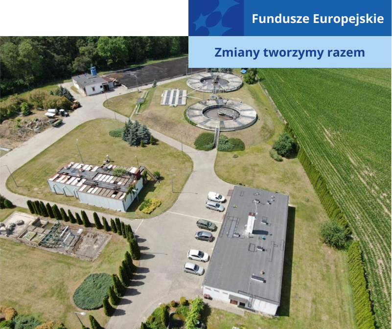 Zdjęcie z lotu ptaka prezentuje oczyszczalnię ścieków. Na terenie znajdują się betonowe budynki o różnych kształtach – kwadratu, prostokąta czy koła. Są też samochody oraz zieleń. Fotografia pochodzi z archiwum beneficjenta.