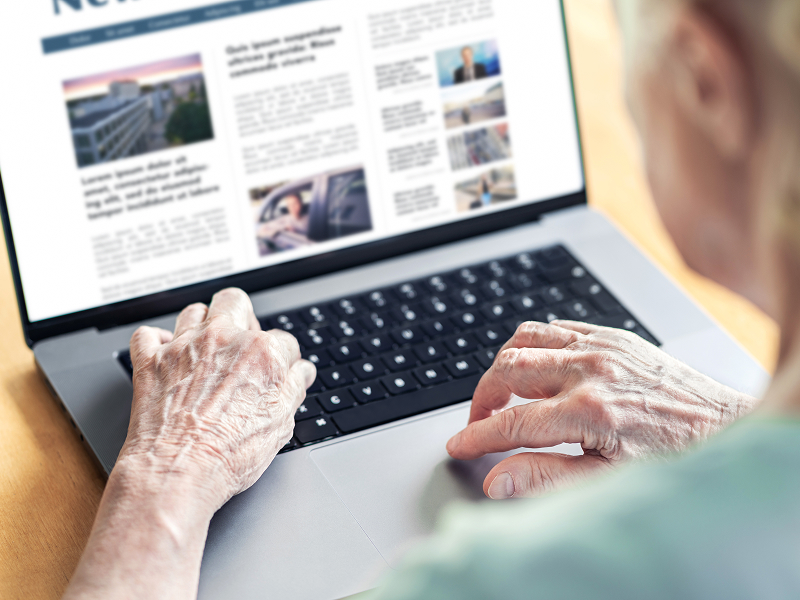 Ilustracja przedstawia starszą osobę przeglądającą internet za pomocą laptopa. Widoczny jest ekran komputera i ręce użytkownika. Zdjęcie pochodzi z adobe stock.