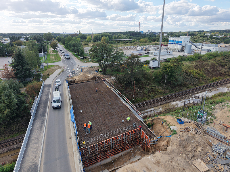 Zdjęcie z lotu ptaka przedstawia budowę mostu. Widoczni są robotnicy oraz pojazdy, przejeżdżające przez zapasową przeprawę. Fotografia pochodzi z archiwum Wielkopolskiego Zarządu Dróg Wojewódzkich.