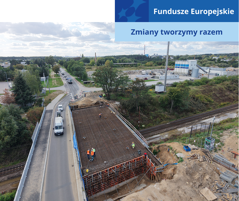 Zdjęcie z lotu ptaka przedstawia budowę mostu. Widoczni są robotnicy oraz pojazdy, przejeżdżające przez zapasową przeprawę. Fotografia pochodzi z archiwum Wielkopolskiego Zarządu Dróg Wojewódzkich.