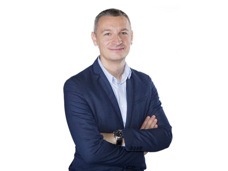 Zdjęcie przedstawia uśmiechniętego mężczyznę w średnim wieku, w garniturze, z założonymi rękami. Fotografia pochodzi z archiwum prywatnego.