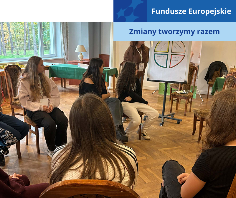 Fotografię wykonano w trakcie szkolenia. Na krzesłach siedzi kilkunastu młodych ludzi. Przed nimi stoi prowadząca szkolenie, która prezentuje na tablicy schemat dotyczący modeli liderstwa. Zdjęcie pochodzi z archiwum beneficjenta.