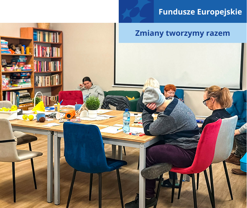 Fotografia przedstawia wnętrze świetlicy, w której przebywa kilka osób. Niektórzy siedzą przy stole, inni na kanapach. Wykonują prace plastyczne. Zdjęcie pochodzi z archiwum Miejskiego Ośrodka Pomocy Rodzinie.