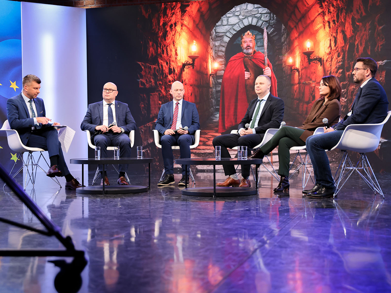 Zdjęcie wykonano podczas gali. Na scenie znajduje się sześć elegancko ubranych osób, w tym pięciu mężczyzn i jedna kobieta. W tle znajduje się ekran, na którym wyświetlona jest flaga Unii Europejskiej oraz postać króla Bolesława Chrobrego w koronie, czerwonej pelerynie, z mieczem, w kamiennym korytarzu. Fotografia pochodzi z archiwum Urzędu Marszałkowskiego Województwa Wielkopolskiego. 