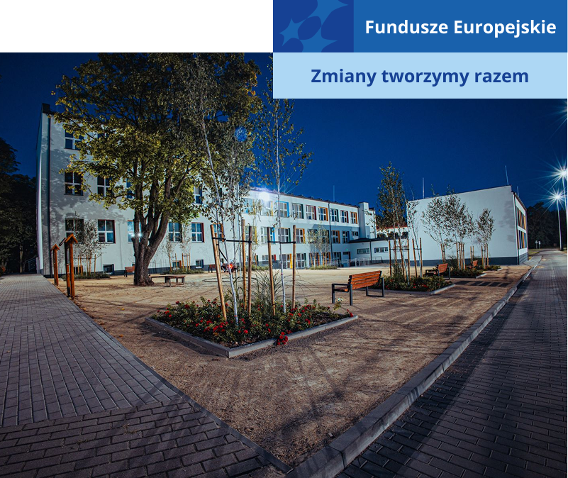 Na zdjęciu wykonanym wieczorową porą widoczny jest gmach szkoły z nową elewacją oraz teren przed nią, z latarniami, ławkami i roślinami. Fotografia pochodzi z archiwum beneficjenta.