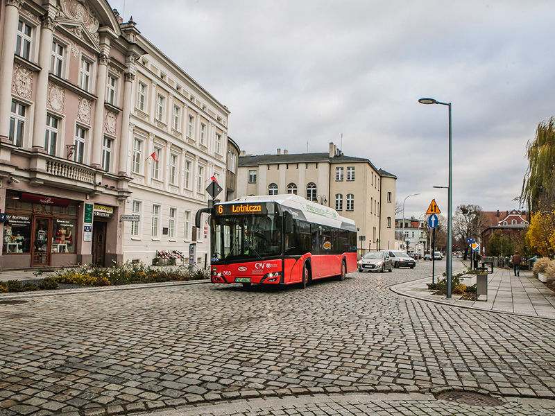 Fotografia przedstawia autobus utrzymany w czerwonych barwach, jadący przez centrum miasta. Zdjęcie pochodzi z archiwum beneficjenta.