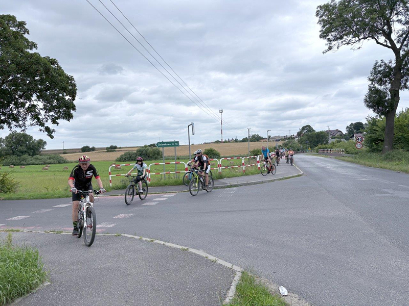 Na zdjęciu widoczni są rowerzyści poruszający się ścieżką rowerową, przecinający drogę. Fotografia pochodzi z archiwum beneficjenta.