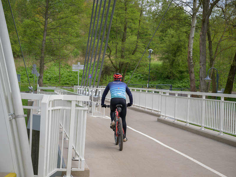 Na zdjęciu widoczny jest rowerzysta w kasku, przejeżdżający przez wiadukt. Autorem fotografii jest Maciej Motylewski.