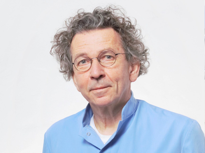 Na zdjęciu znajduje się mężczyzna w średnim wieku, o siwych kręconych włosach, w okrągłych okularach i jasnoniebieskiej koszulce. Fotografia pochodzi z archiwum prywatnego.