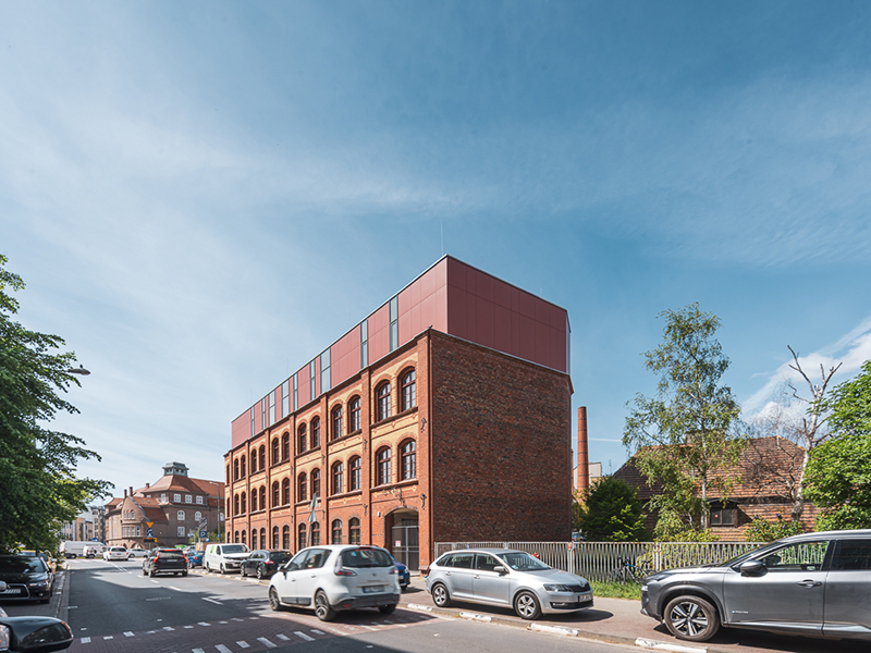 Na zdjęciu widoczny jest budynek w kształcie prostopadłościanu. Prawie wszystkie kondygnacje są ceglane, za wyjątkiem ostatniej, stworzonej w nowoczesnym stylu. Fotografia pochodzi z archiwum beneficjenta.