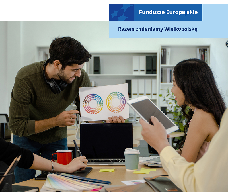 Zdjęcie przedstawia czwórkę młodych osób – dwie kobiety i dwóch mężczyzn pracujących nad projektem w firmie. Jeden z mężczyzn trzyma schemat, pozostali przyglądają się. Widoczne są rzeczy na stole: laptop, przybory do pisania. Fotografia pochodzi z adobe stock.