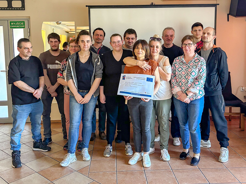 Zdjęcie przedstawia uczestników projektu unijnego. Grupa kilkunastu kobiet i mężczyzn pozuje, uśmiechając się. Fotografia pochodzi z archiwum archiwum Miejsko-Gminnego Ośrodka Pomocy Społecznej w Kępnie.