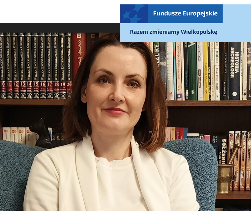 Zdjęcie przedstawia uśmiechniętą kobietę w średnim wieku, w eleganckim ubraniu. Siedzi w fotelu na tle książek. Fotografia pochodzi z archiwum prywatnego.