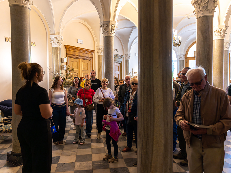 Zdjęcie przedstawia grupę turystów w pałacowym wnętrzu, na czele z przewodniczką. Widoczne są między innymi masywne, ozdobne filary budynku. Zdjęcie pochodzi z archiwum Departamentu Polityki Regionalnej Urzędu Marszałkowskiego Województwa Wielkopolskiego.
