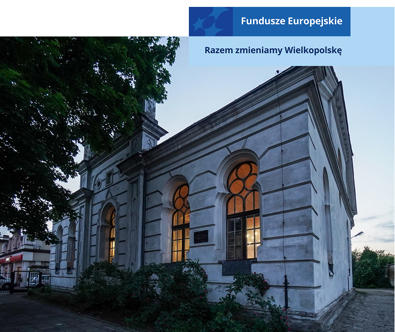 Zdjęcie przedstawia niewielki budynek dawnej synagogi, o jasnej elewacji. W środku świeci się światło. Fotografia pochodzi z archiwum beneficjenta.