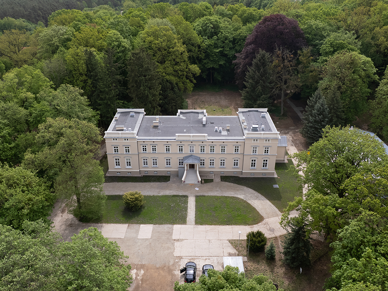 Fotografia z lotu ptaka przedstawia pałac położony w parku, porośniętym drzewami. Zdjęcie pochodzi z archiwum Urzędu Marszałkowskiego Województwa Wielkopolskiego.