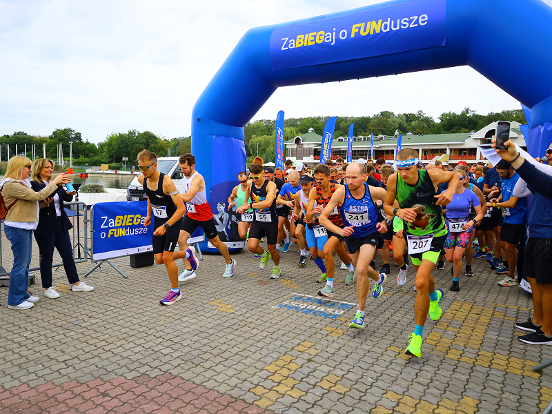 Na zdjęciu widoczny jest start biegu. Kilkudziesięciu zawodników w sportowych strojach rusza, przebiegając przez dmuchaną bramkę z napisem zabiegaj o fundusze. Fotografia pochodzi z archiwum Urzędu Marszałkowskiego Województwa Wielkopolskiego.
