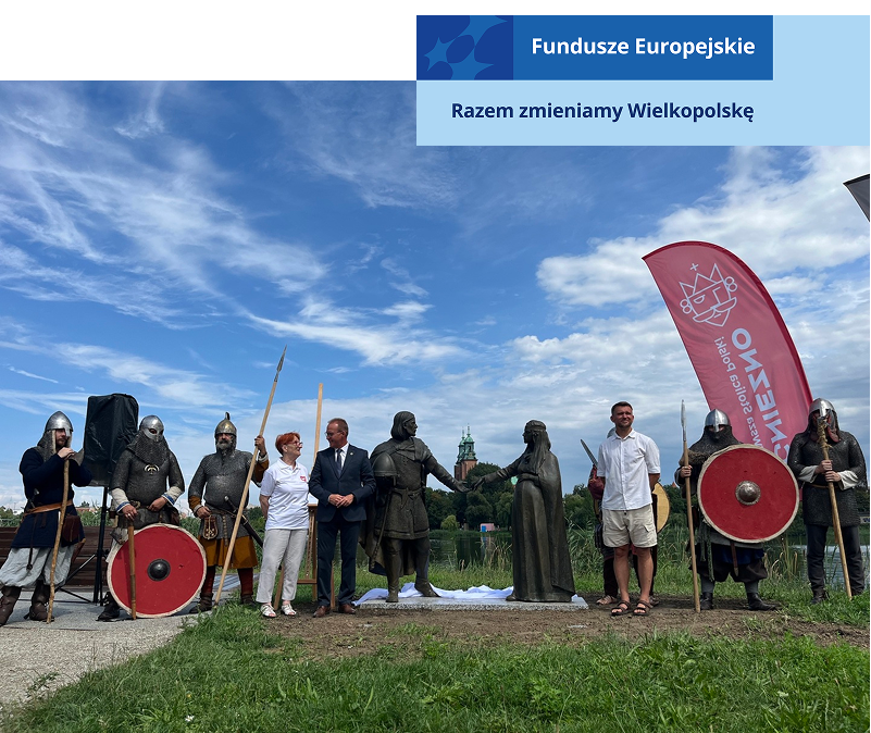 Przy rzeźbach Mieszka I i Dobrawy pozują ludzie. Niektórzy ubrani są w codzienne ubrania, inni przebrani są za rycerzy. Fotografia pochodzi z archiwum beneficjenta.