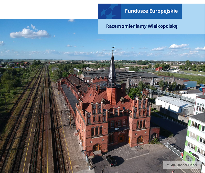 Fotografia z lotu ptaka przedstawia dworzec kolejowy, przypominający nieco w swojej budowie pałac – ma strzelistą wieżę, jest z czerwonej cegły. Z lewej znajdują się tory kolejowe, po prawej zaś zabudowania miejskie. Autorem zdjęcia jest Aleksander Liebert.