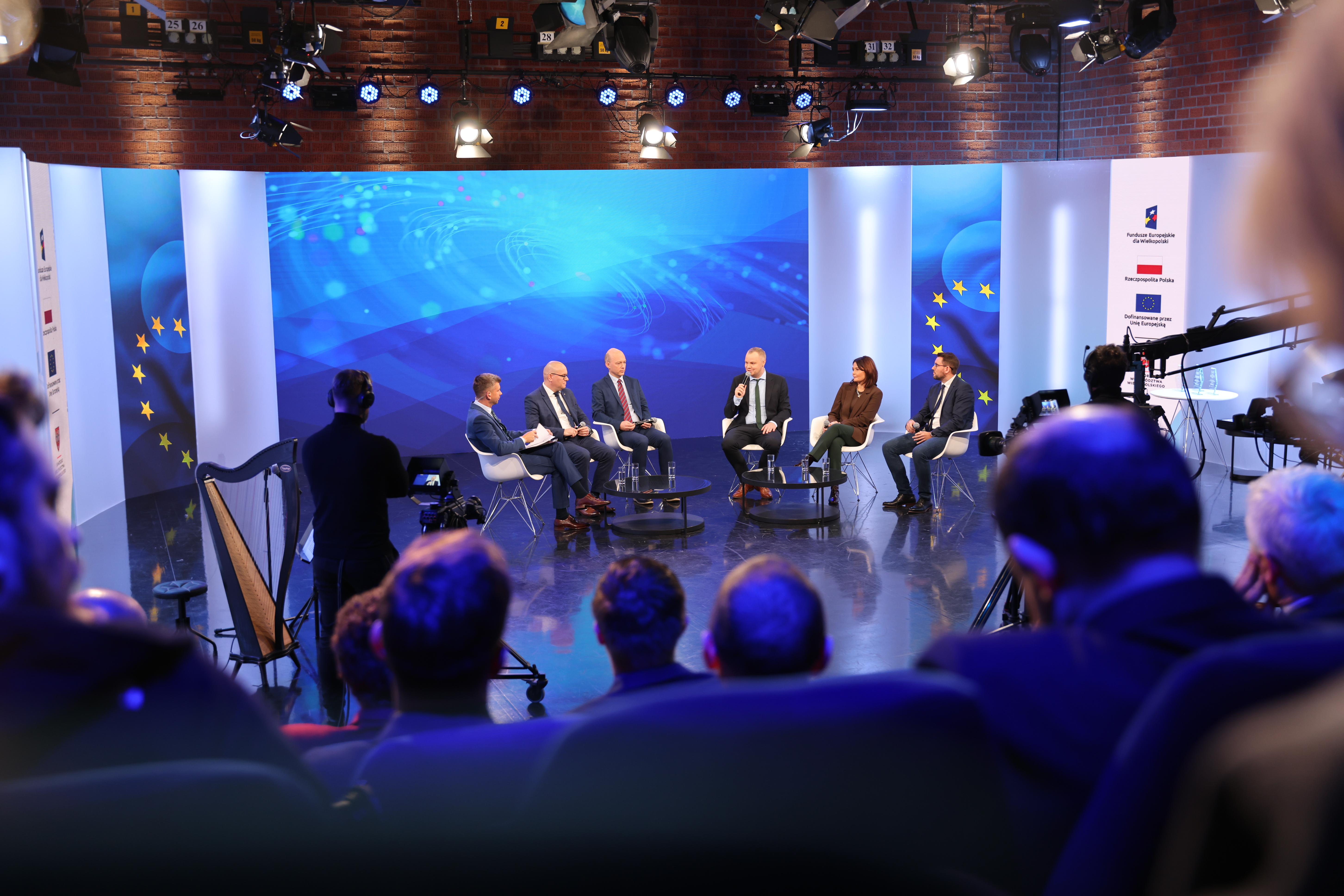 Z oddali widać sześć osób rozmawiających na scenie