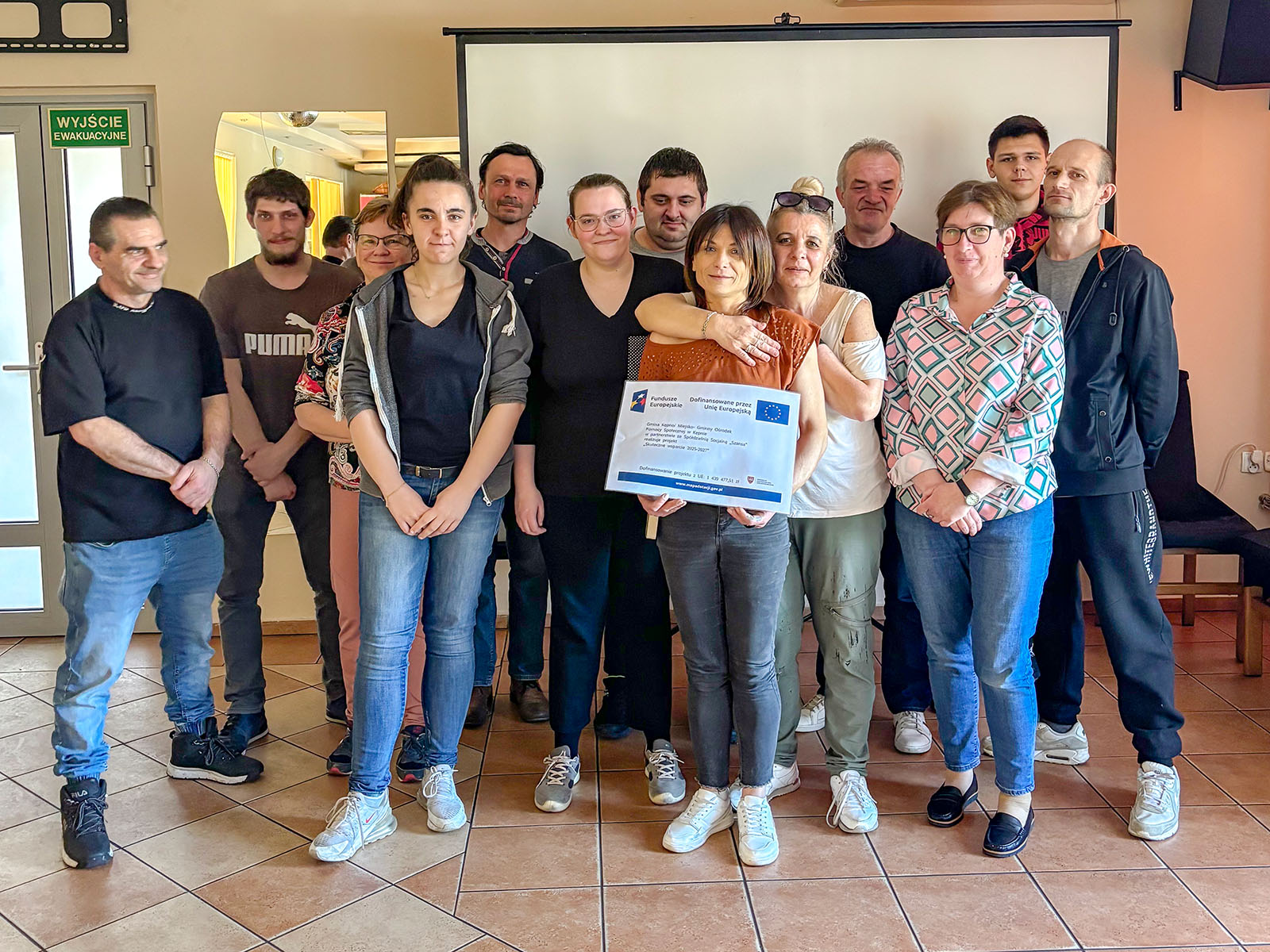 Na zdjęciu kilka osób, które trzyma tabliczkę z oznaczeniem Fundusze Europejskie 