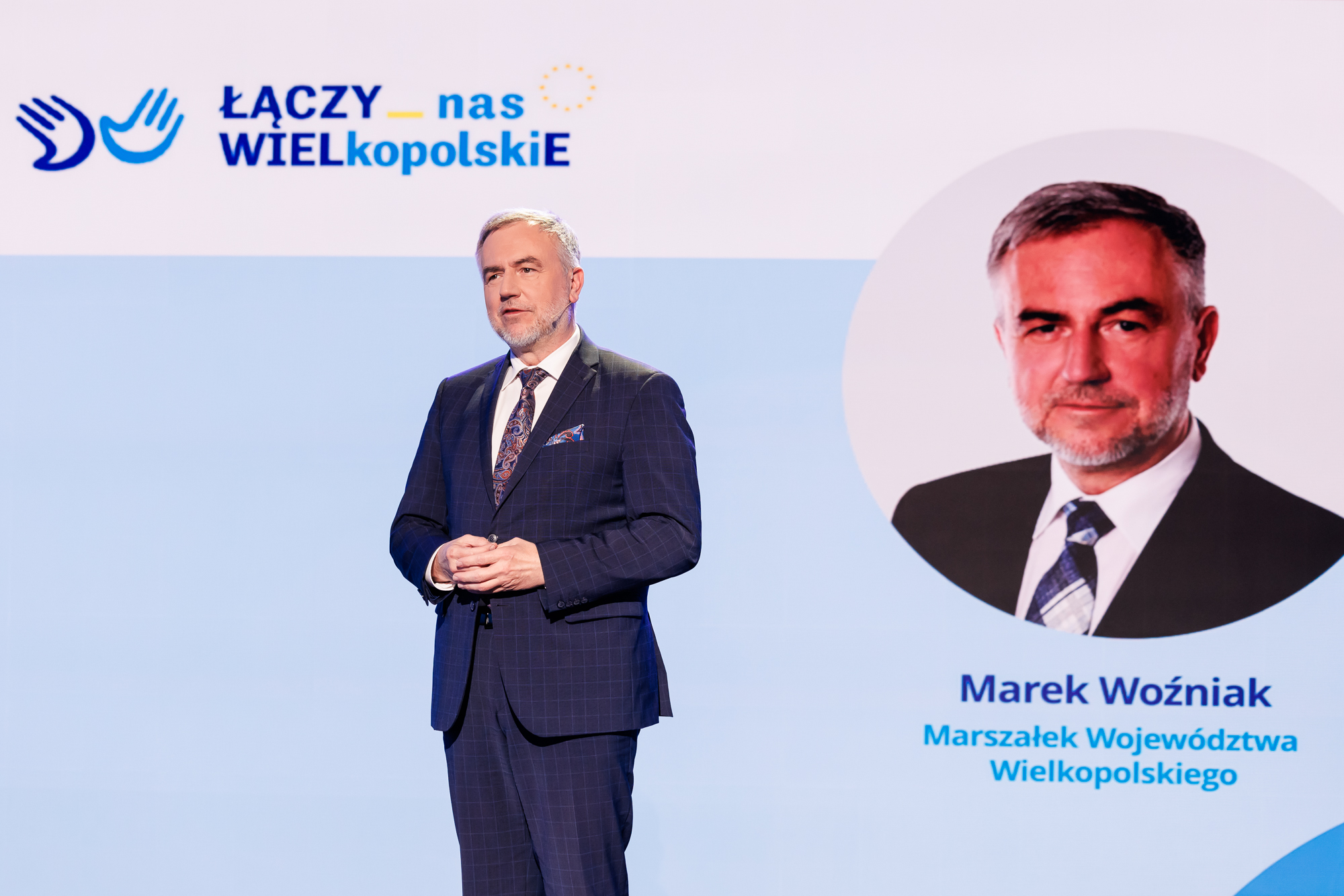 Na zdjęciu stoi mężczyzna w tle jego zdjęcie i napis Łączy nas WIELkopolskiE