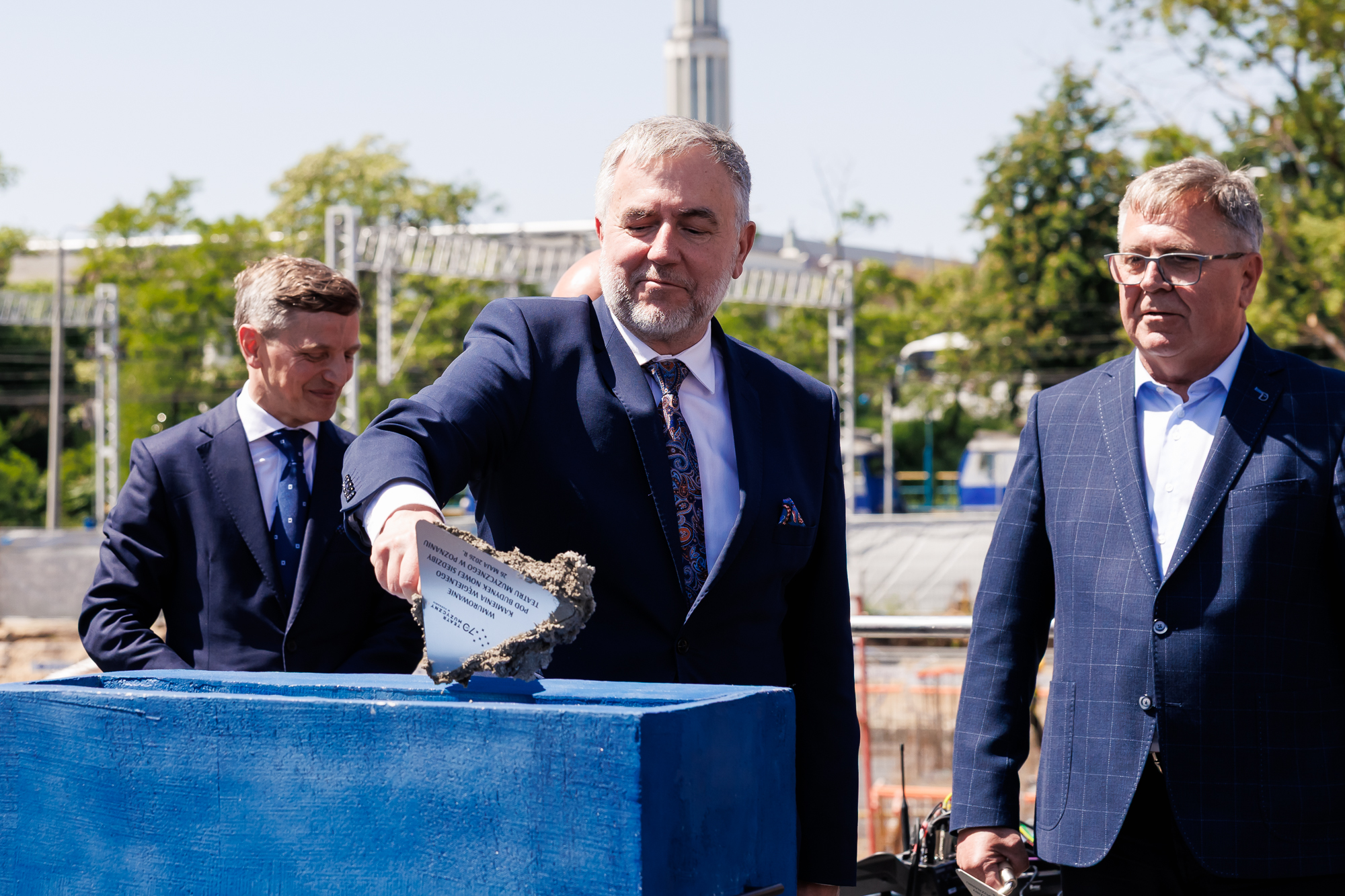 Na zdjęciu trzech mężczyzn ubranych w garnitury, w tle widok na maisto