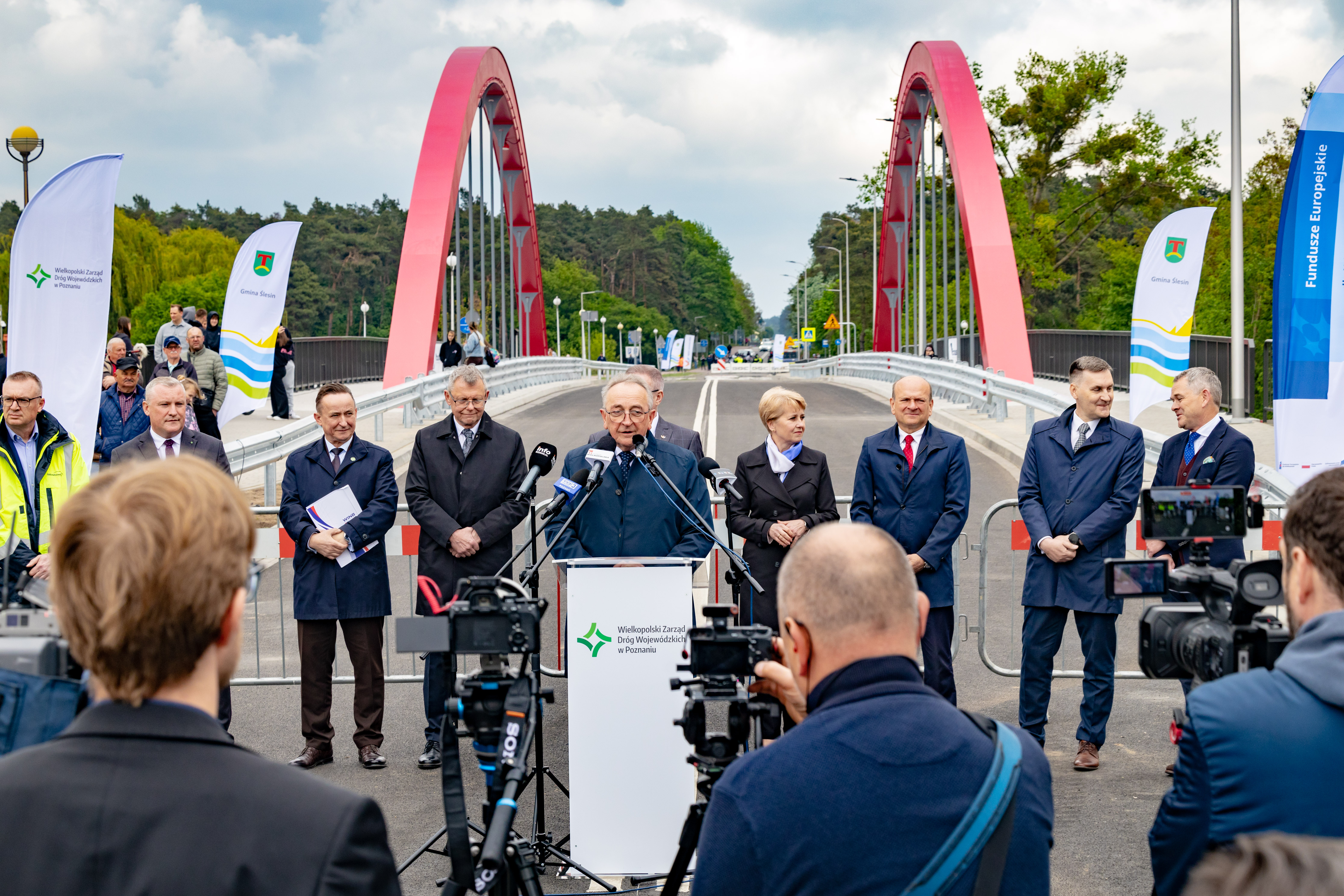 Na zdjęciu kilka osób stojących obok mównicy, w tle widok na most
