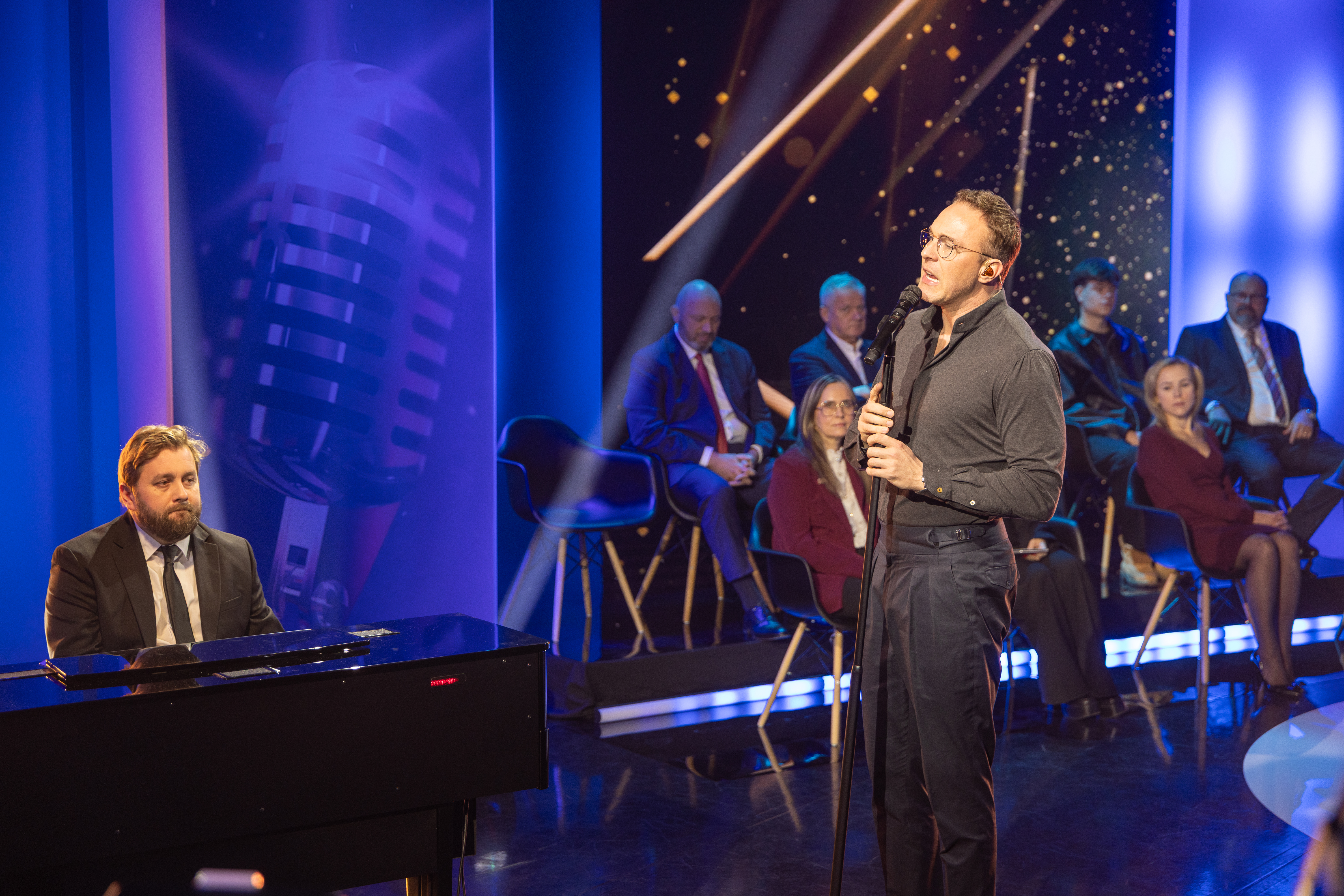 Na zdjęciu dwóch muzyków: jeden śpiewa, drugi gra na fortepianie 