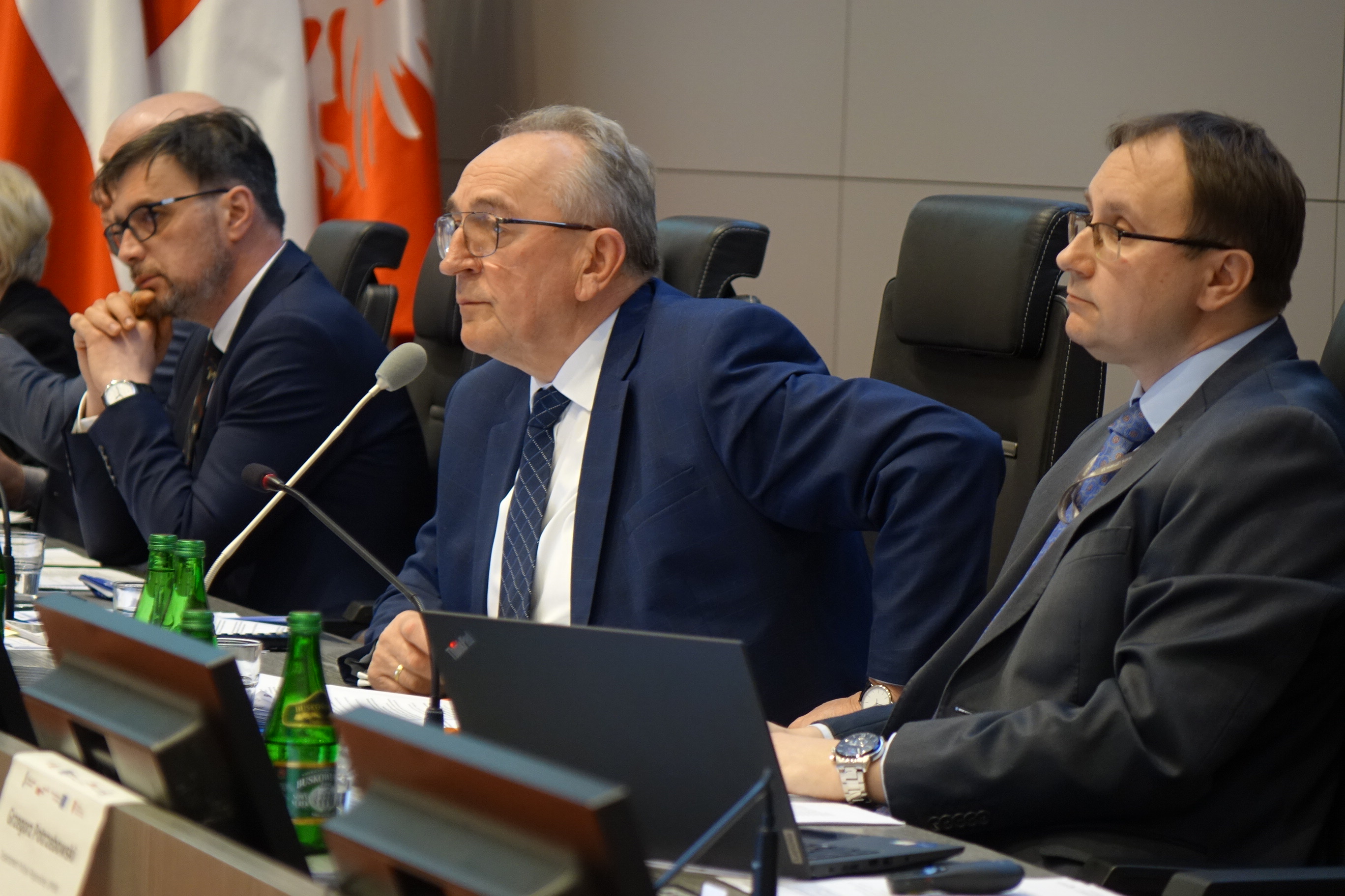 Na zdjęciu trzech mężczyzn ubranych w garnitury, którzy przysłuchują się dyskusji 