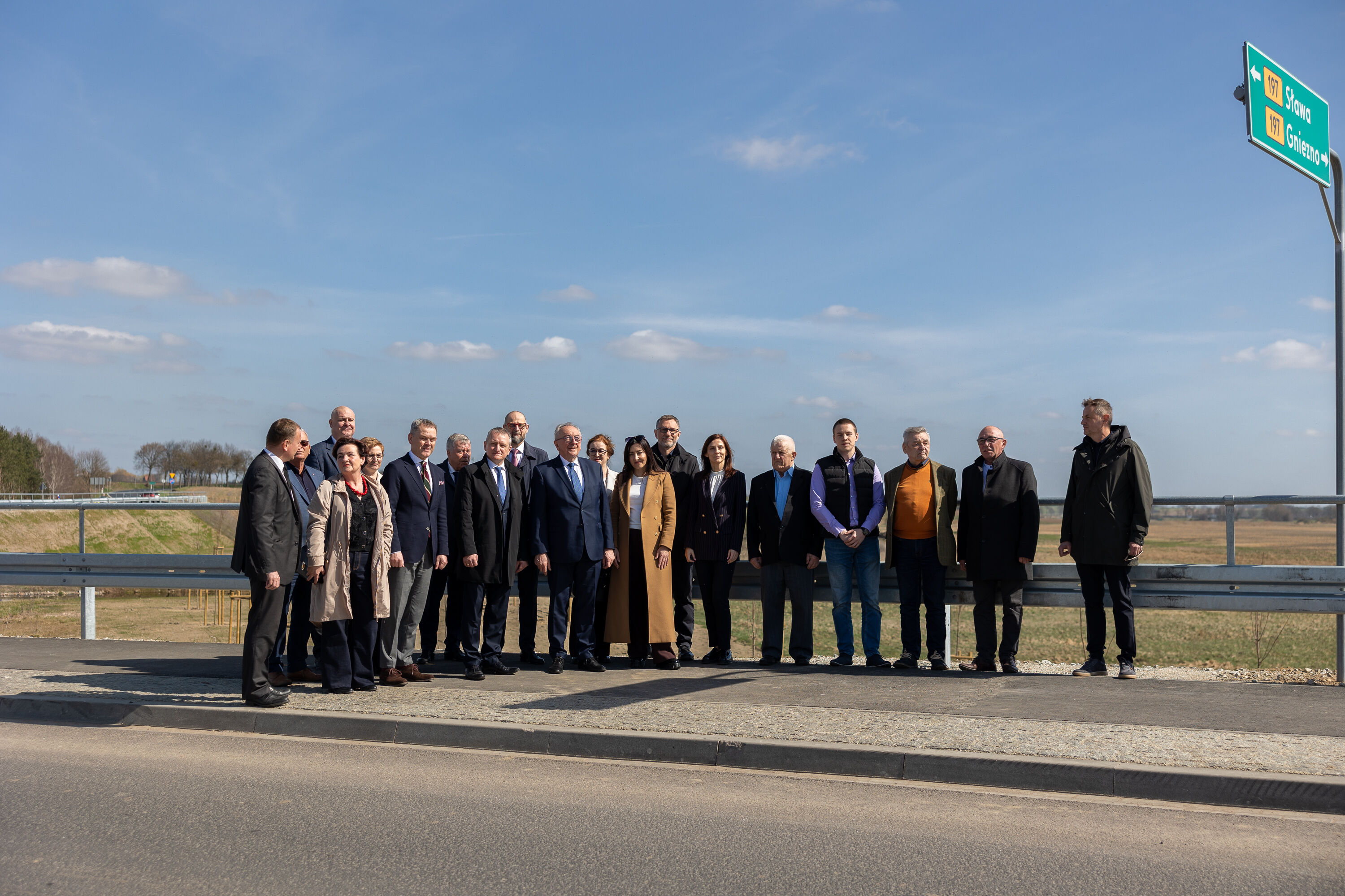 Na zdjęciu kilkanaście osób stojących przy drodze, w tle czyste niebo 