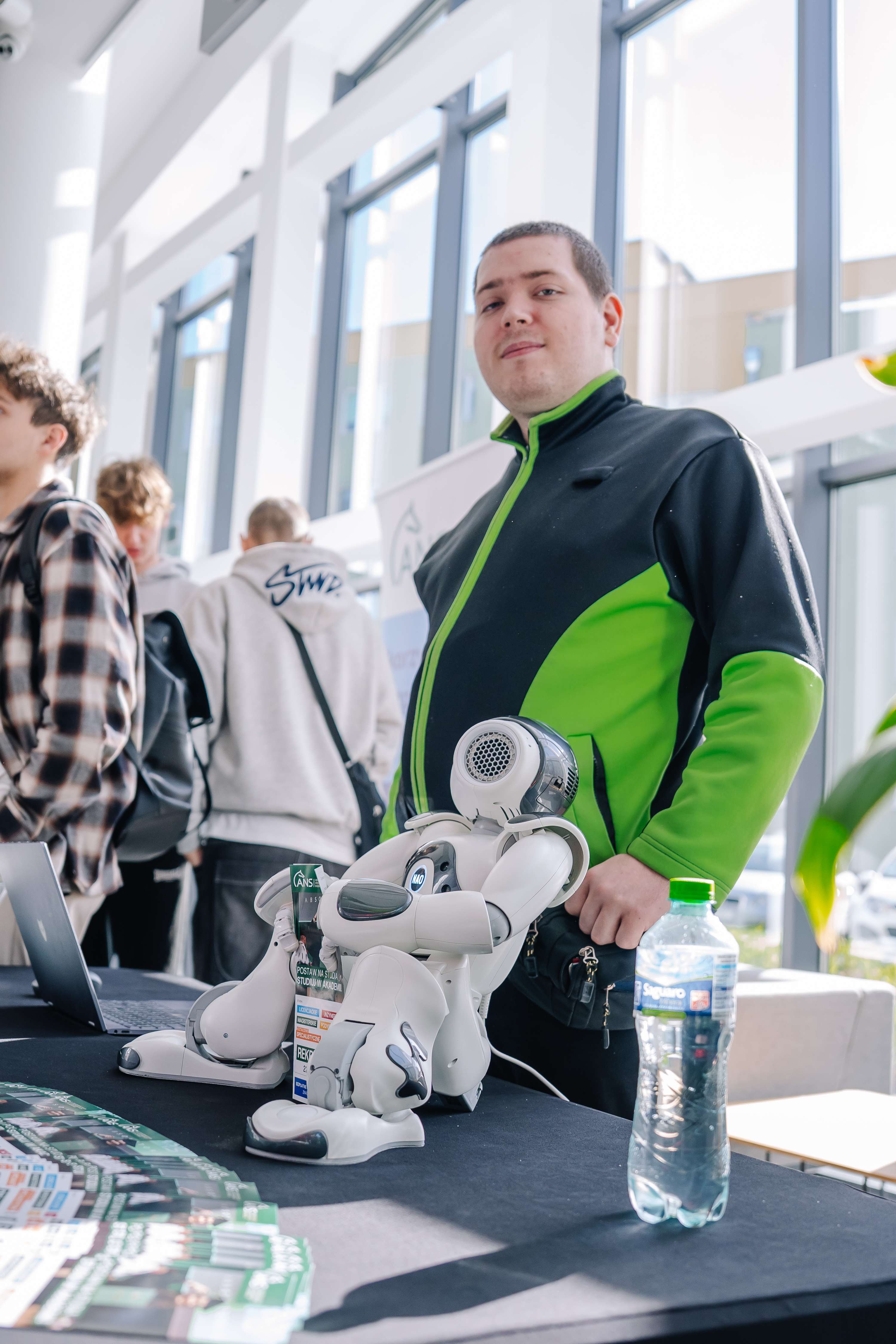 Uśmiechnięty młody chłopak w zielonej bluzie, jest o niego oparty robot 