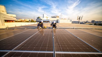 Grafika przedstawia instalację paneli słonecznych na dachu przez dwóch techników.