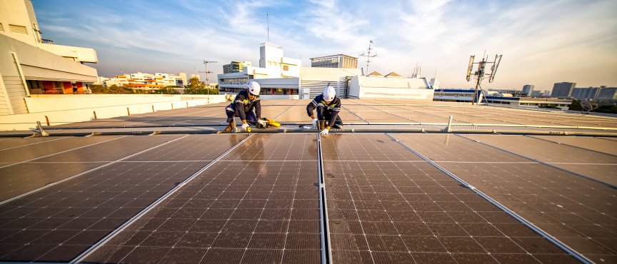 Grafika przedstawia instalację paneli słonecznych na dachu przez dwóch techników.