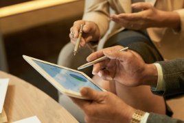 Dwie osoby siedzą z tabletem, pokazują coś długopisem na ekranie