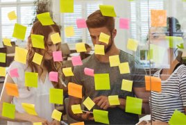 dwie osoby stoją przy przezroczystej tablicy z karteczkami