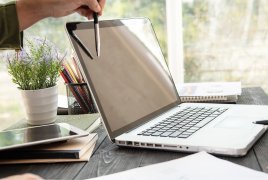 Dłonie z długopisami wskazującymi coś na otwartym laptopie