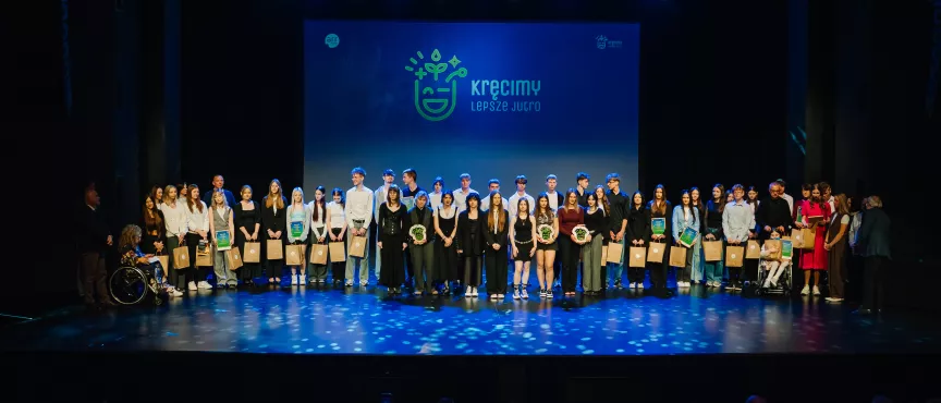 Na zdjęciu kilkanaście osób stojących na scenie, w tle napis "kręcimy lepsze jutro"