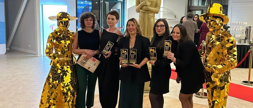 Na zdjęciu pięć uśmiechniętych kobiet, obok stoją posągi 