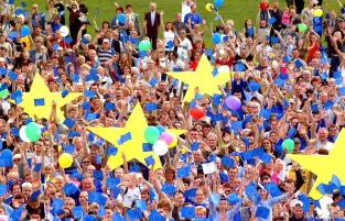 Na zdjęciu tłum ludzi trzymający żółte gwiazdy i niebieskie balony