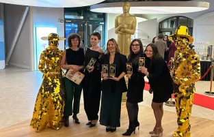 Na zdjęciu pięć uśmiechniętych kobiet, obok stoją posągi 