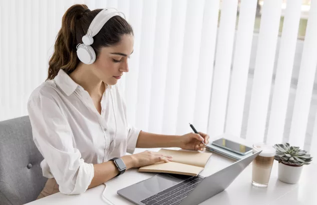 Kobieta z słuchawkami przed laptopem na szkoleniu online