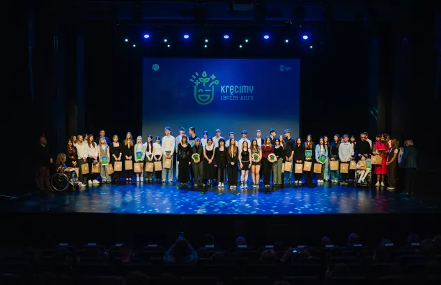 Na zdjęciu kilkanaście osób stojących na scenie, w tle napis "kręcimy lepsze jutro"