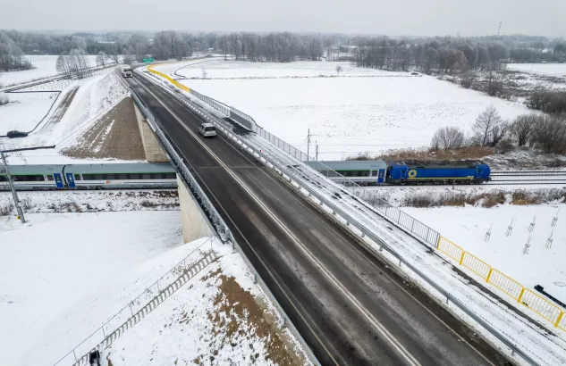 Na zdjęciu widok z lotu ptaka na zaśnieżony wiadukt, a pod nim przejeżdża pociąg