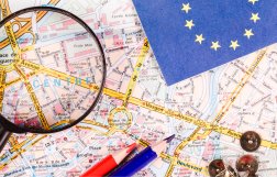 lupa, kredki i chorągiewka z flagą Unii Europejskiej połozone na mapie