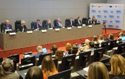 Na zdjęciu widać stół prezydialny z ośmioma osobami i kilknaście osób siedzący po drugiej stronie